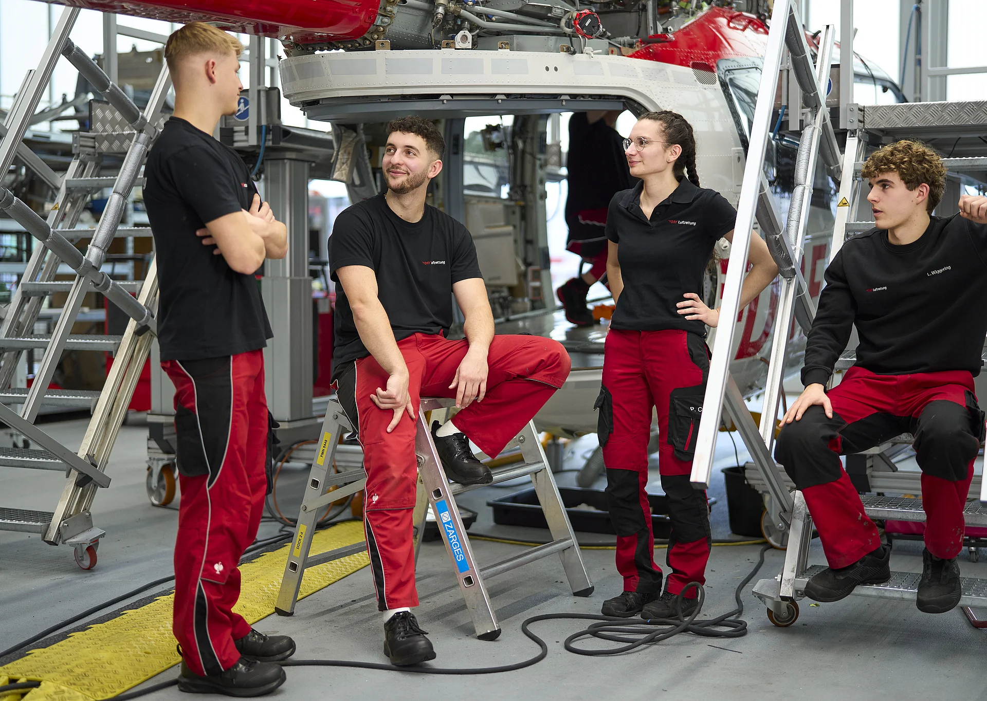 Vier Auszubildende im Bereich Technik der DRF Luftrettung unterhalten sich und stehen in der Werft.