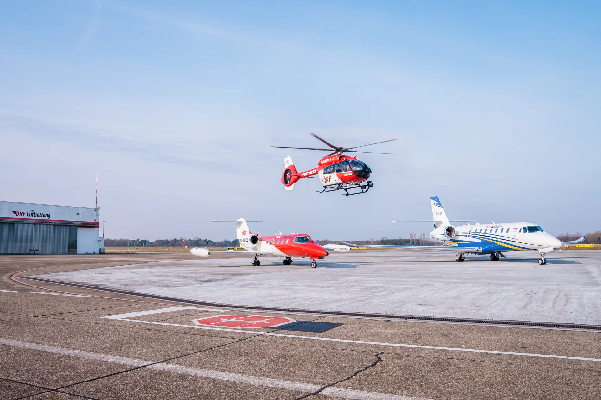 Hubschrauber und Ambulanzflugzeuge der DRF Luftrettung auf dem Vorfeld eines Flughafens