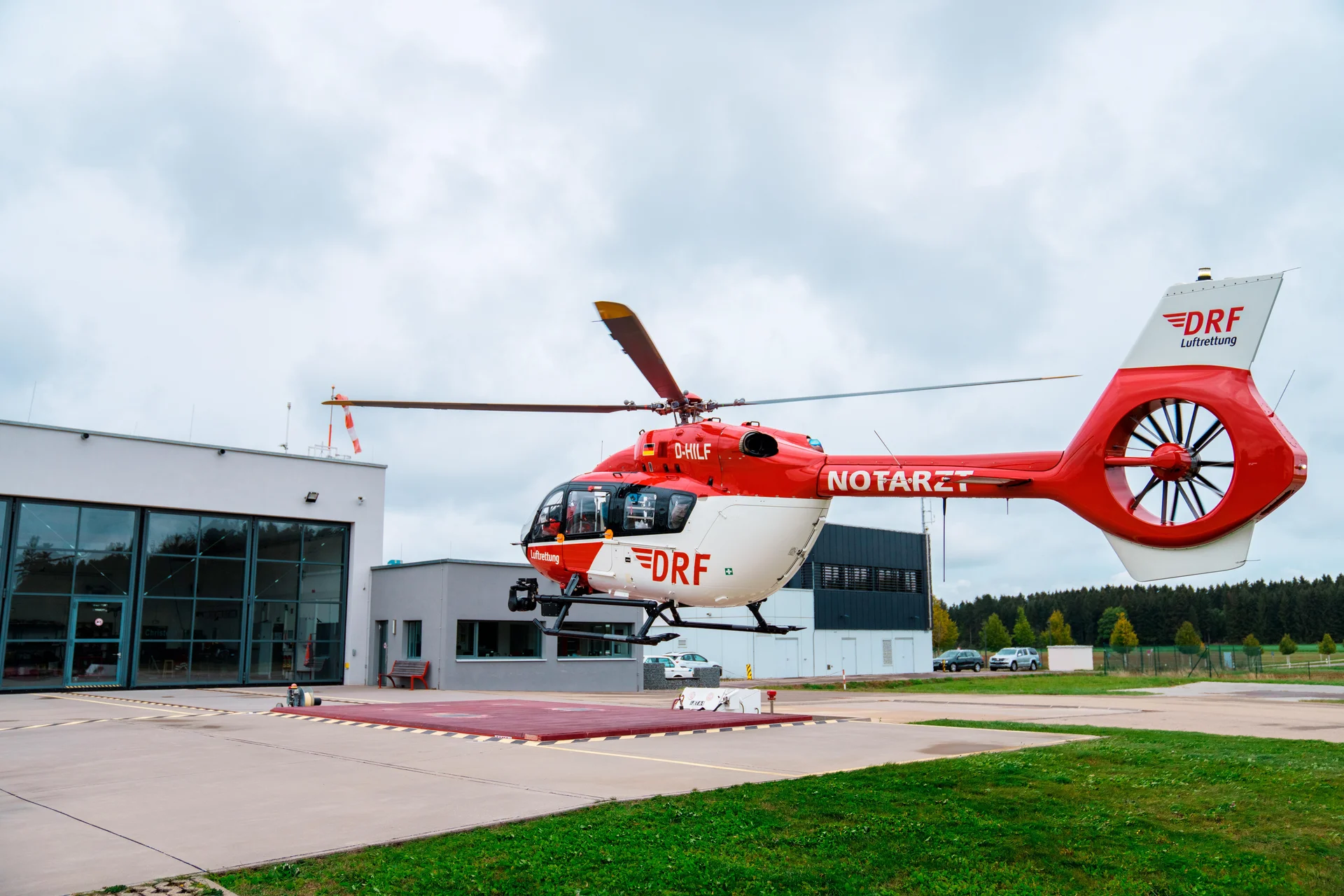 Ein rot-weißer Rettungshubschrauber steht vor einem Hangar.