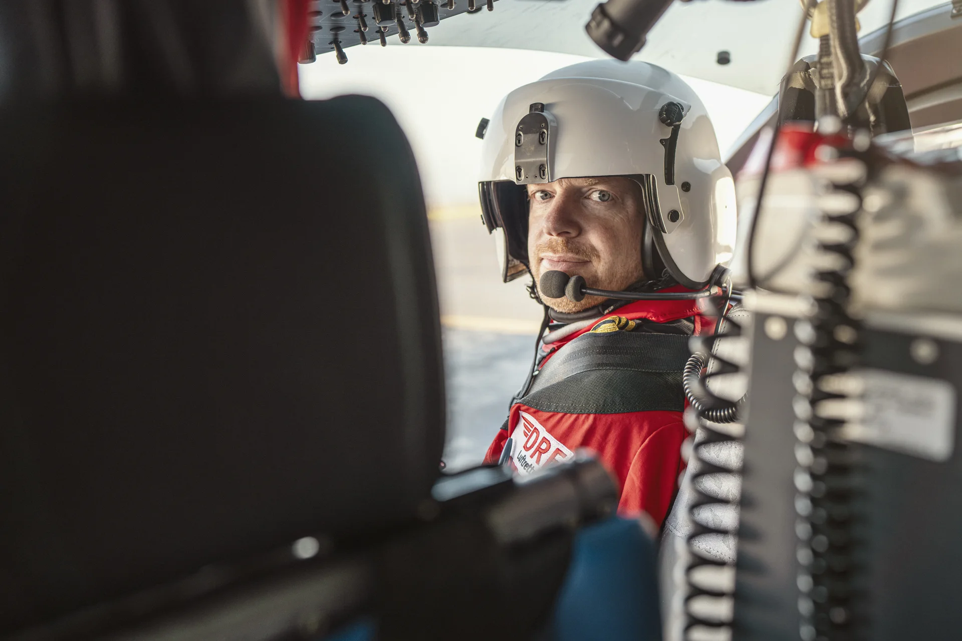 Ein Pilot der DRF Luftrettung sitzt im Cockpit eines Hubschraubers und blickt nach hinten zwischen den Sitzen durch.