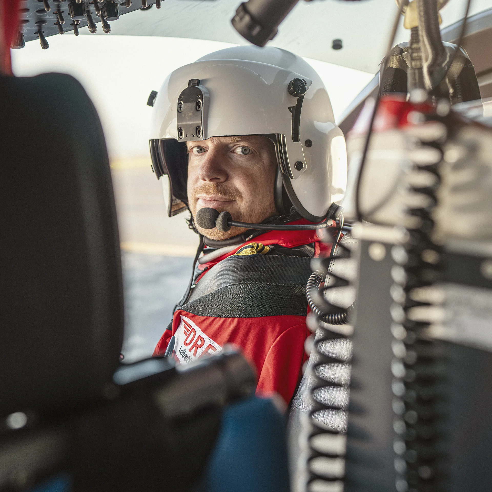 Ein Pilot der DRF Luftrettung sitzt im Cockpit eines Hubschraubers und blickt nach hinten zwischen den Sitzen durch.
